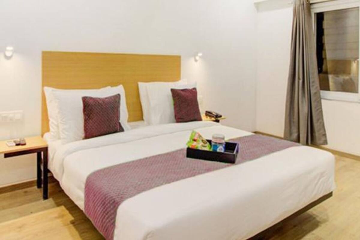 A neatly arranged hotel room with a large bed, a bedside table, and a window with curtains.