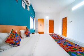 A hotel room with a bed, colorful pillows, a wooden headboard, a hallway with a patterned carpet, and a door with a wooden panel. - FabHotel Virksham Thrivyn (Coimbatore)