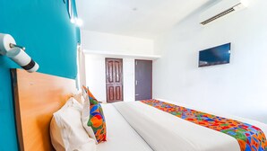A hotel room with a bed, a wooden headboard, a colorful bedspread, a white wall, a flat-screen TV, and a door. - FabHotel Virksham Thrivyn (Coimbatore)