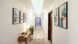 A hallway with framed abstract art, a wooden console table with a plant, and a potted plant. - FabHotel Taj Residency (New Delhi)