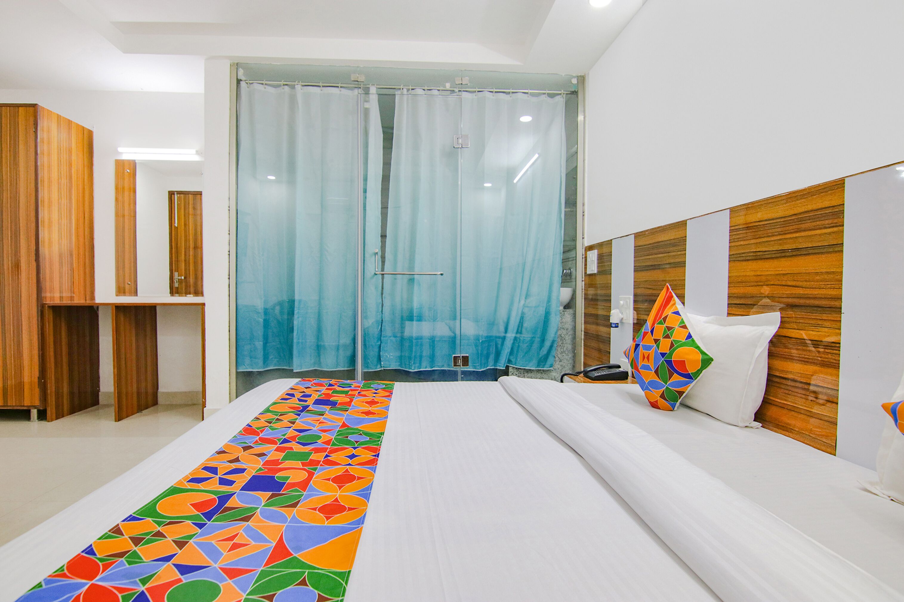 A hotel room with a large bed, a wooden headboard, a shower with a glass door, and a colorful rug.