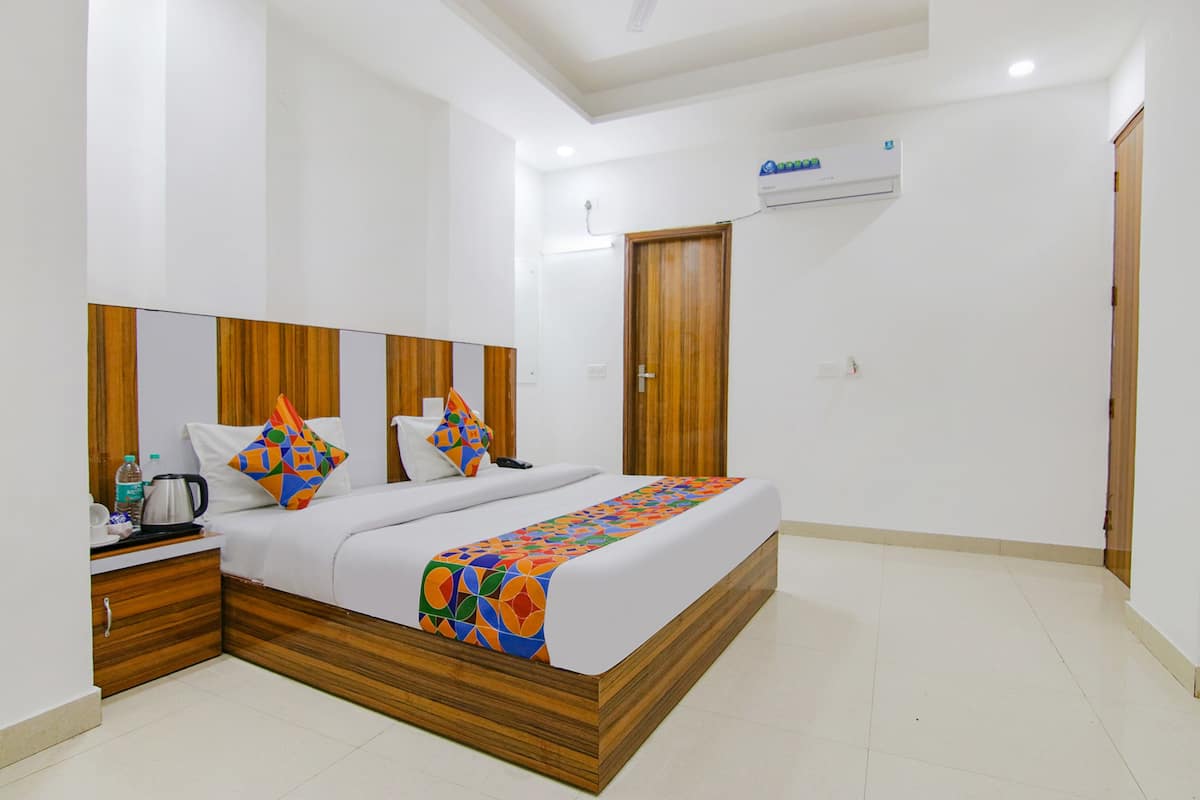 A modern hotel room with a wooden headboard, a bed with colorful bedding, a nightstand with a kettle, and a wooden wardrobe.