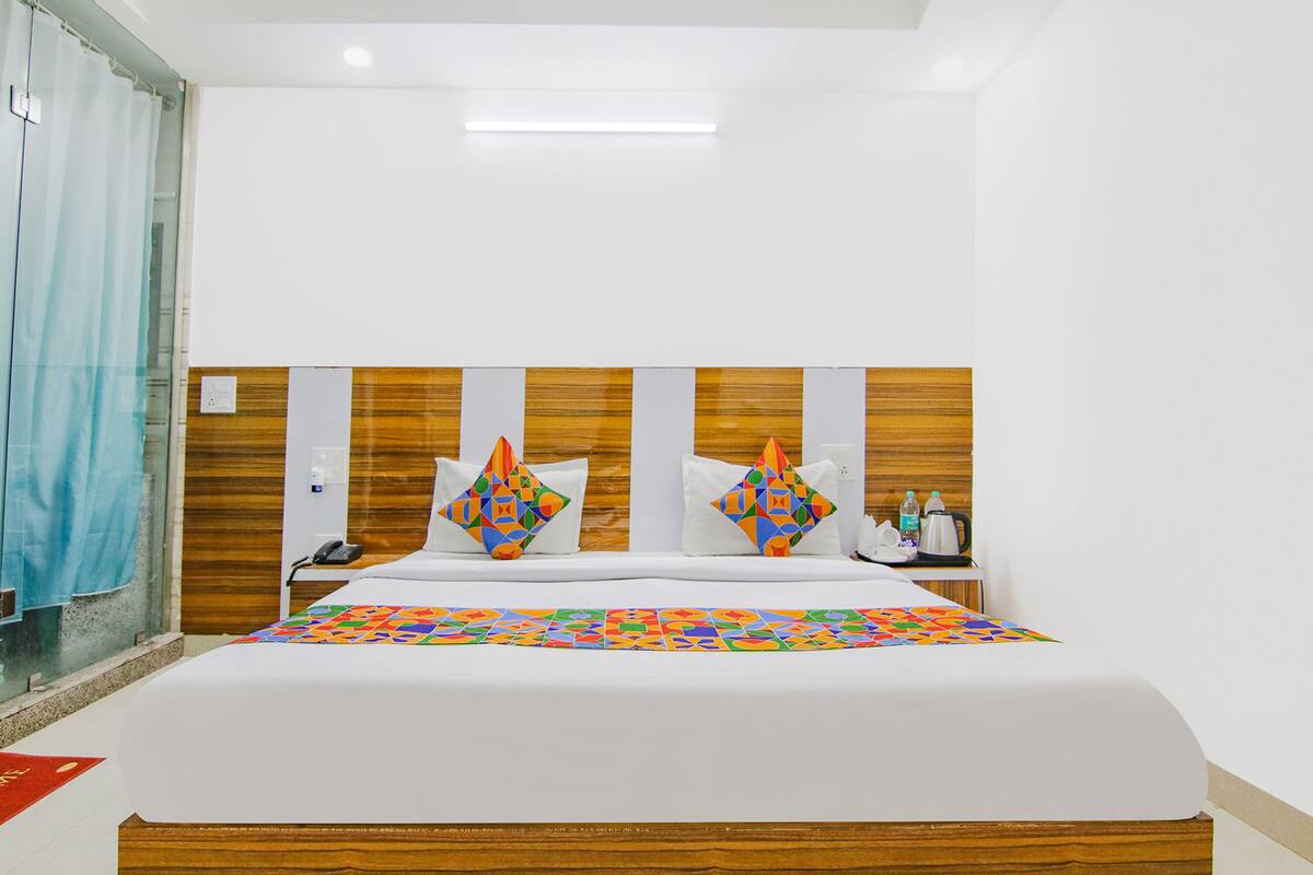 A hotel room with a large bed, wooden headboard, a telephone, and a small table with a kettle and bottles.