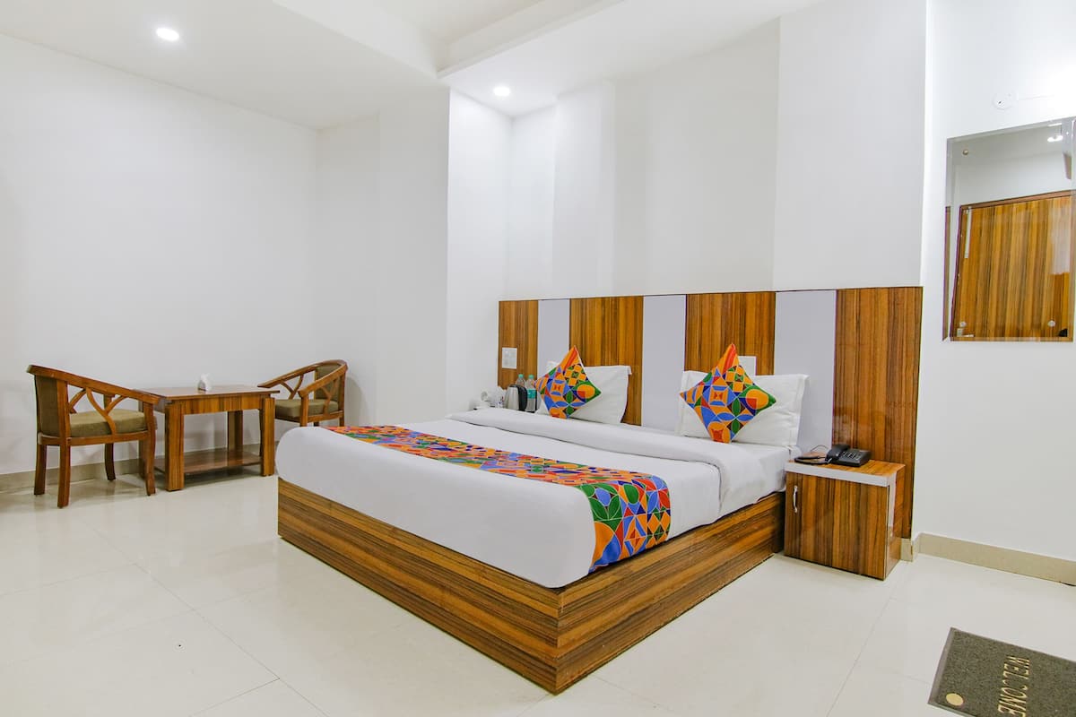 A hotel room with a wooden bed frame, a desk with chairs, a bedside table, and a mirror on the wall.