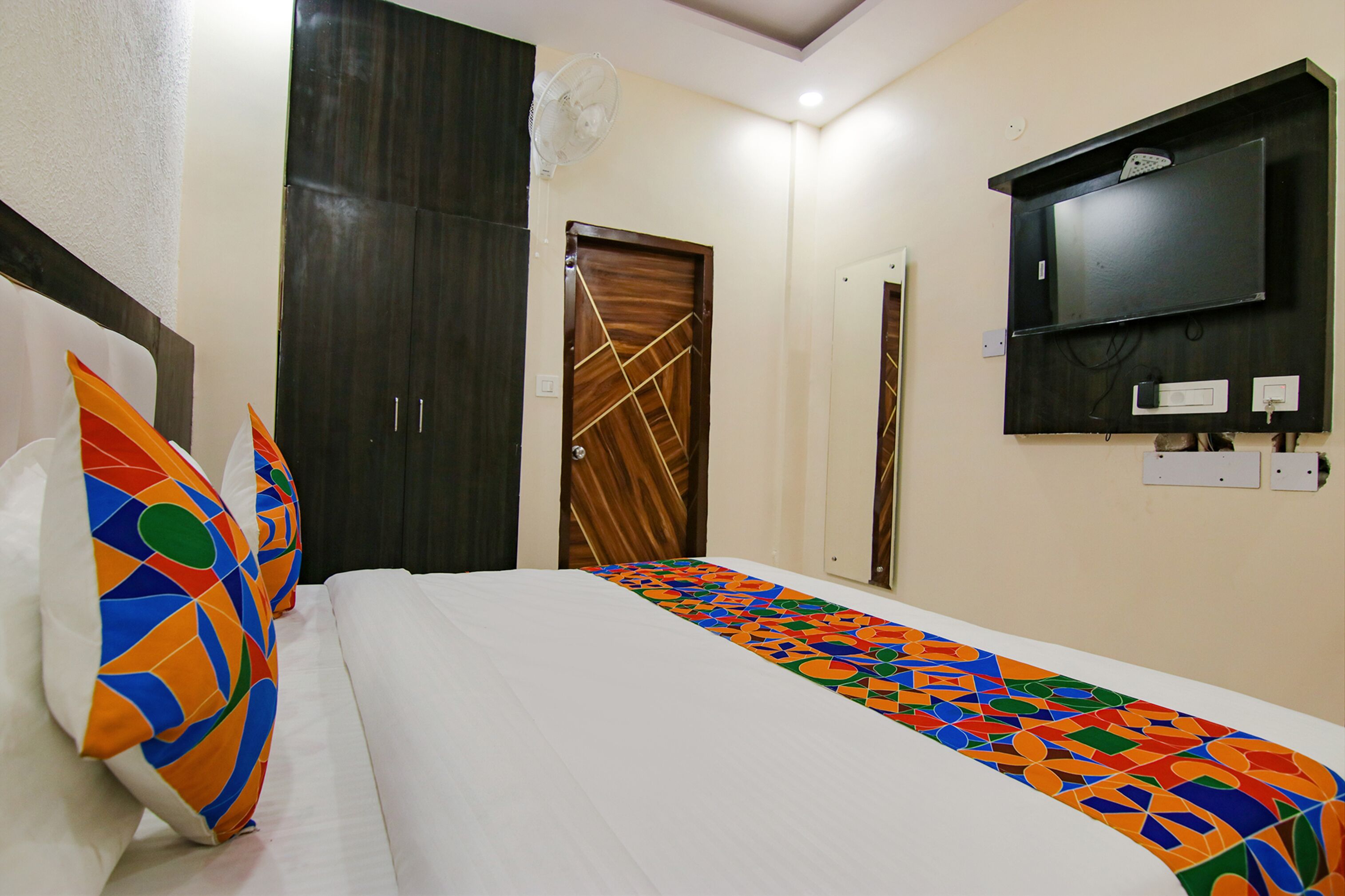 A hotel room with a bed, colorful pillows, a TV, and a wardrobe.