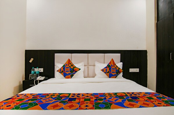 A bed with a white headboard, two pillows with geometric patterns, a colorful geometric-patterned bedspread, a nightstand with a phone, and a water bottle.
