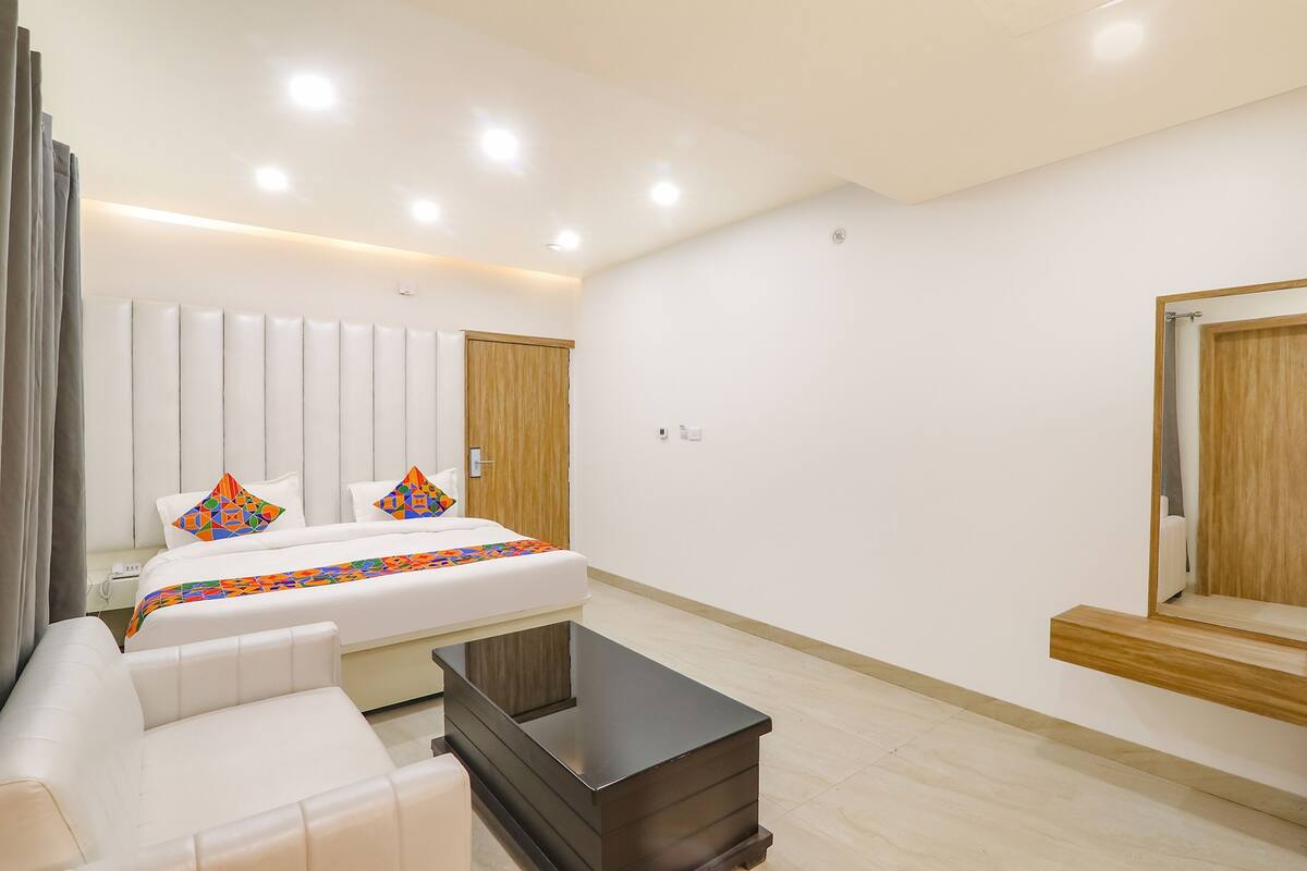 A modern hotel room with a bed, a sofa, a small table, and a mirror.