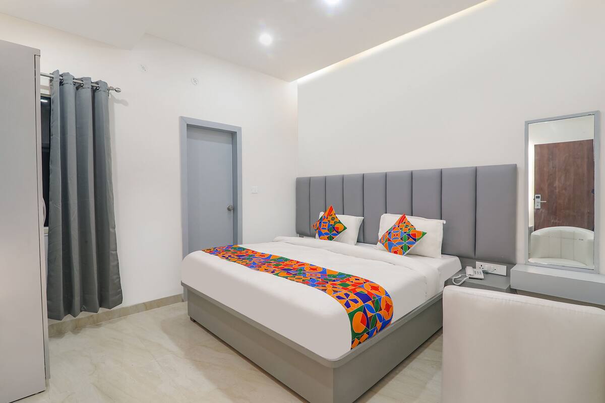 A modern bedroom with a bed, grey headboard, white bedding, and a colorful throw blanket.