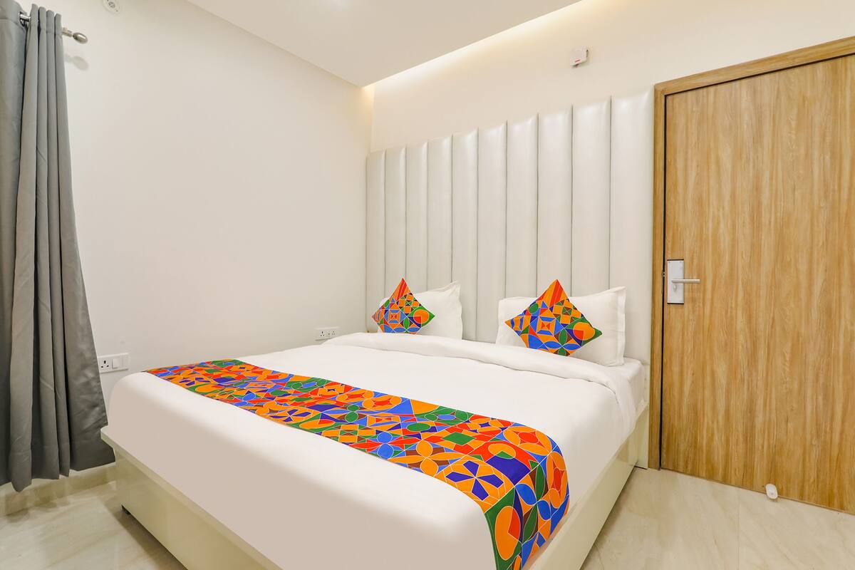 A modern hotel room with a large bed, a wooden door, and a white headboard.