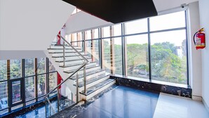 Un intérieur moderne avec un escalier en verre menant à un balcon, de grandes fenêtres et un extincteur fixé au mur.