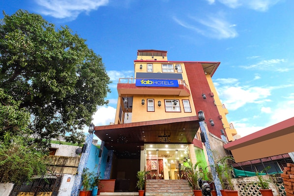 A multi-story building with a 'fab hotels' sign, a staircase leading to the entrance, and potted plants around the entrance area.