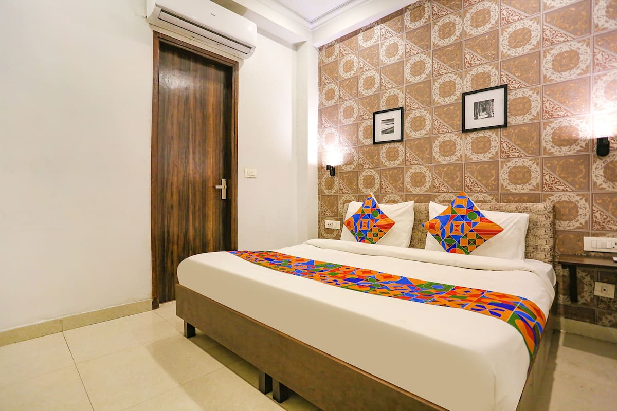 A hotel room with a large bed, a wooden door, patterned wallpaper, and two wall-mounted light fixtures.