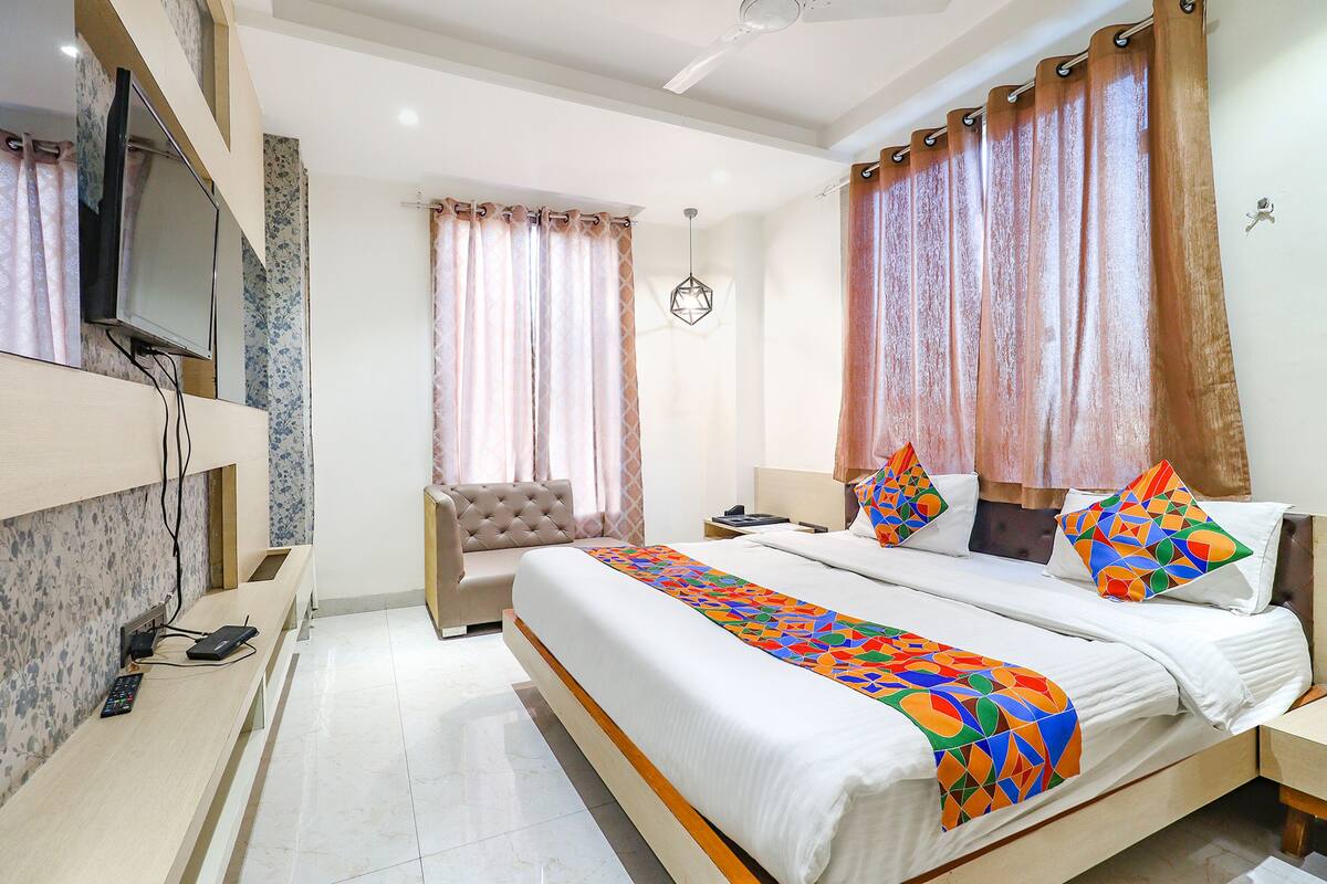 Une chambre d’hôtel comprenant un lit, un téléviseur fixé au mur, un bureau avec une chaise et une fenêtre avec des rideaux.