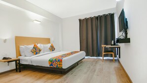 A hotel room with a bed, a desk, a chair, a TV, and a curtain. - FabHotel Infinity Stays (Gurugram)