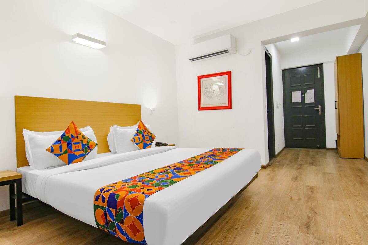 Habitaci ón de hotel con una cama grande, cabecera de madera, mesita de noche, un cuadro en la pared y una puerta a la derecha.