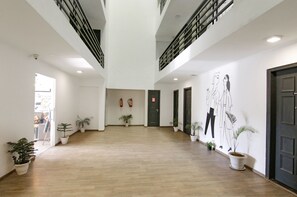 A spacious, well-lit hallway with wooden flooring, potted plants, and a black door at the end.