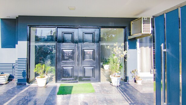 A modern building entrance with a dark-colored double door, potted plants, and a green mat on the ground. - FabHotel Infinity Stays (Gurugram)