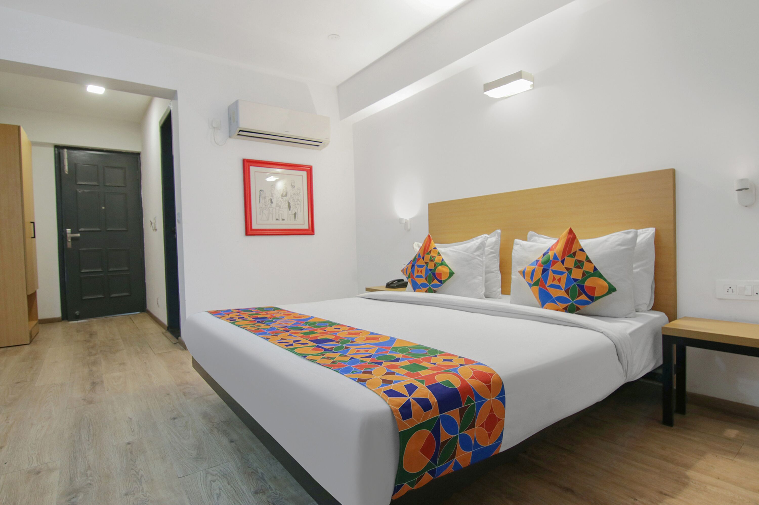 A hotel room with a large bed, a wooden headboard, a bedside table, and a door leading to another room.