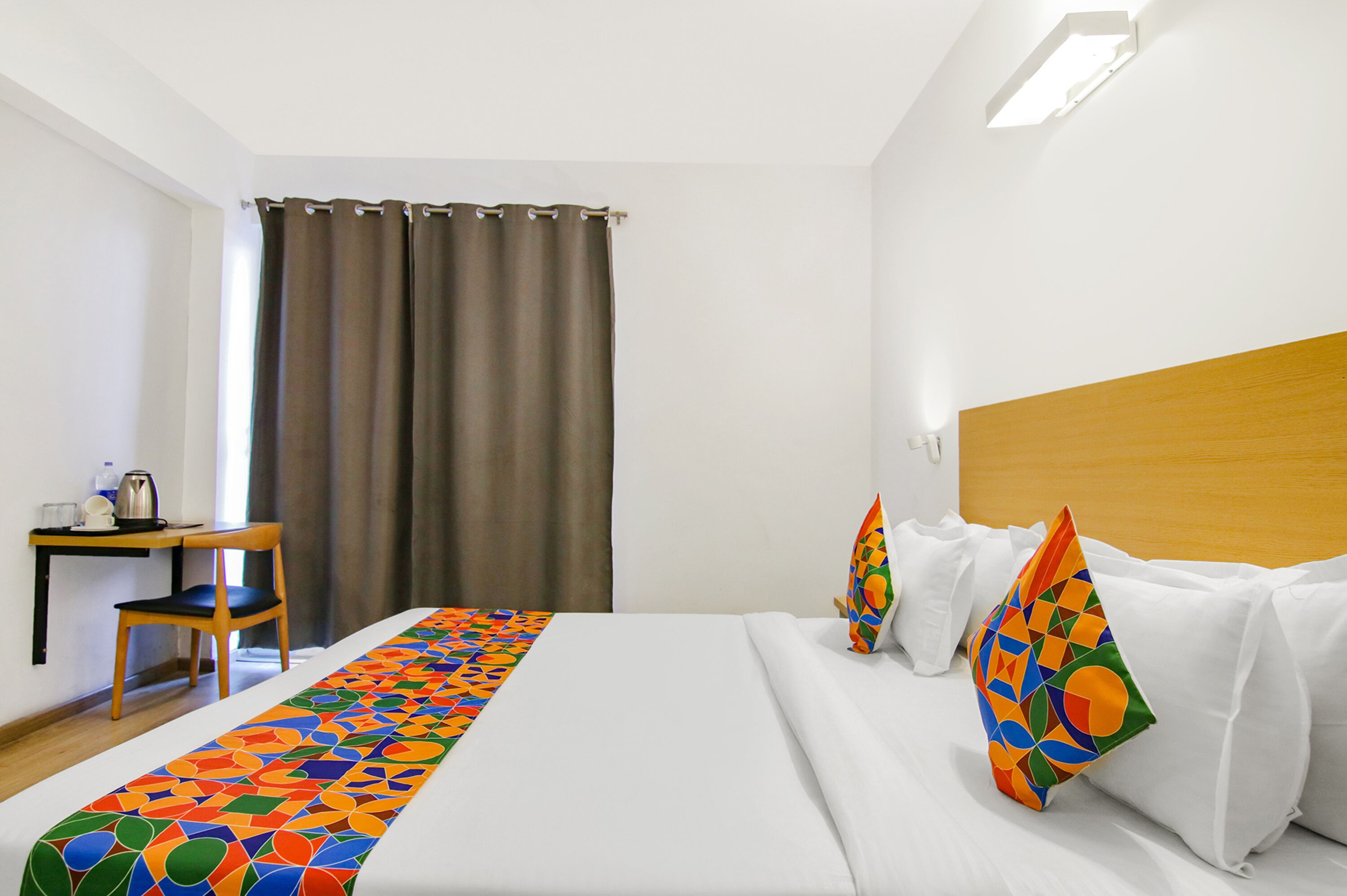 A hotel room with a bed, a desk, a chair, and a window with curtains.