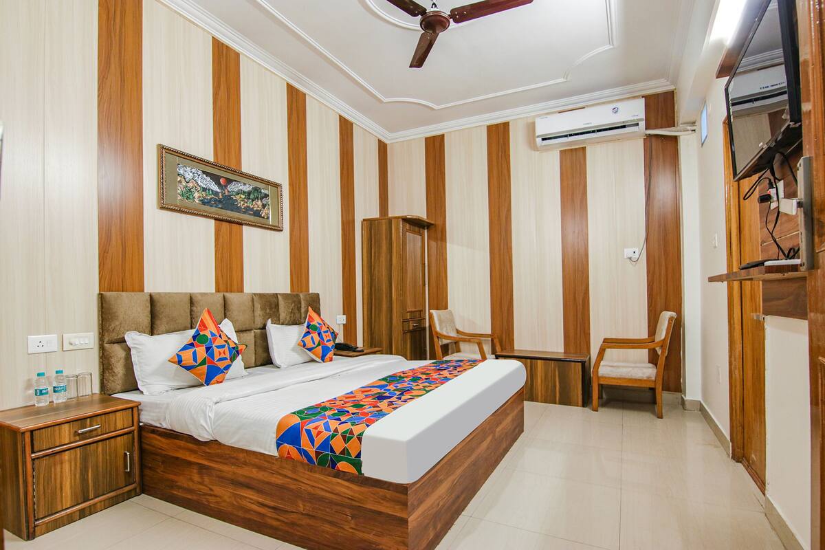 A hotel room with a wooden bed, a bedside table, a chair, a desk, a ceiling fan, and an air conditioning unit.