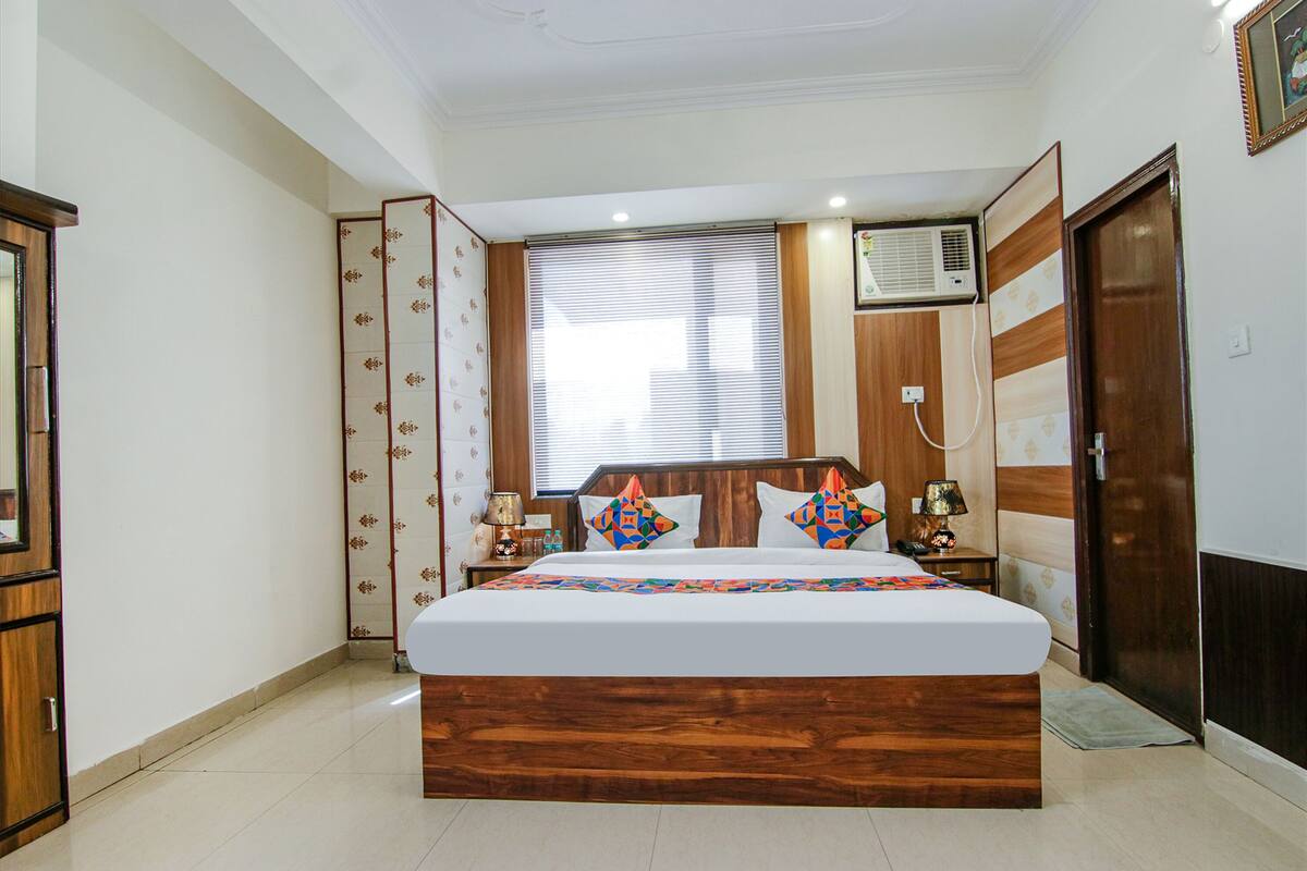 A bedroom with a wooden bed, a window with blinds, an air conditioning unit, and a door.