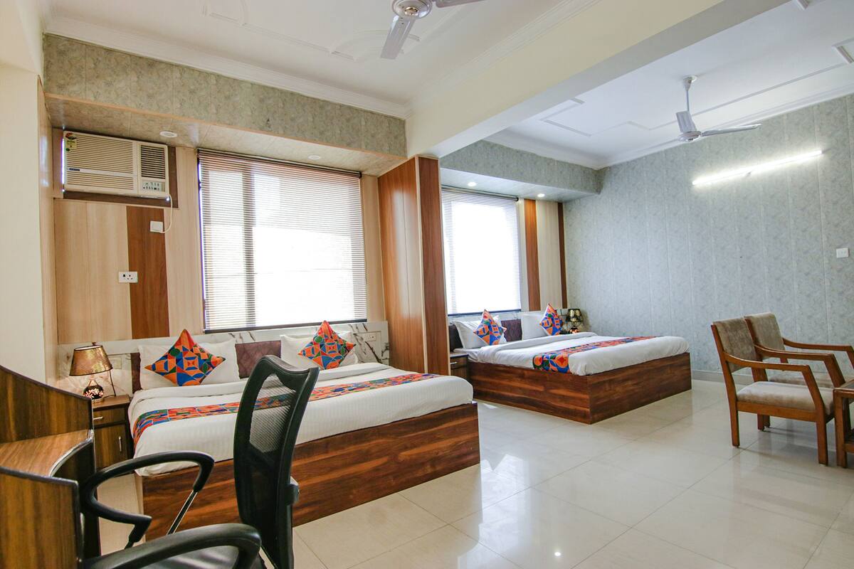A hotel room with two beds, a desk, a chair, and a ceiling fan.