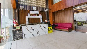 Zona de recepción de hotel con mostrador de mármol, un sofá rojo y una pared de madera.