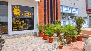 Un hotel llamado "Vistara Grand" con un cartel que enumera servicios como habitaciones, restaurante, salón de banquetes, salón de conferencias, salón de fiestas y salón para reuniones privadas.