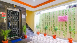 Área interna com piso ladrilhado, plantas em vasos, uma escada e uma parede com plantas penduradas.