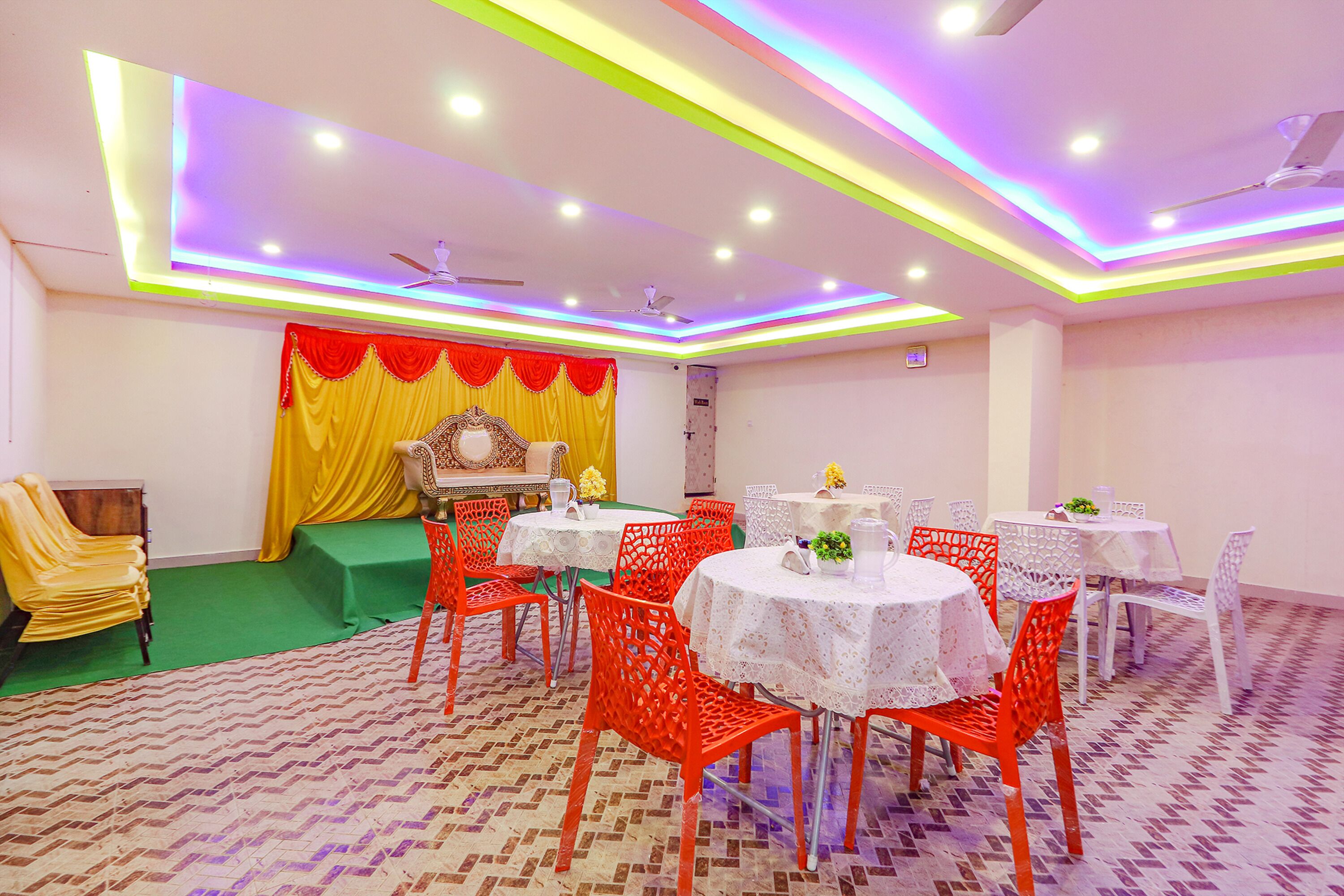 A banquet hall with round tables, red chairs, and a stage with a golden backdrop.