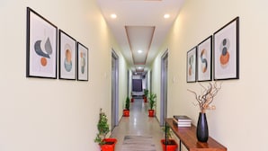 Um corredor com quadros de arte abstrata nas paredes, plantas em vasos e um console de madeira com um vaso.