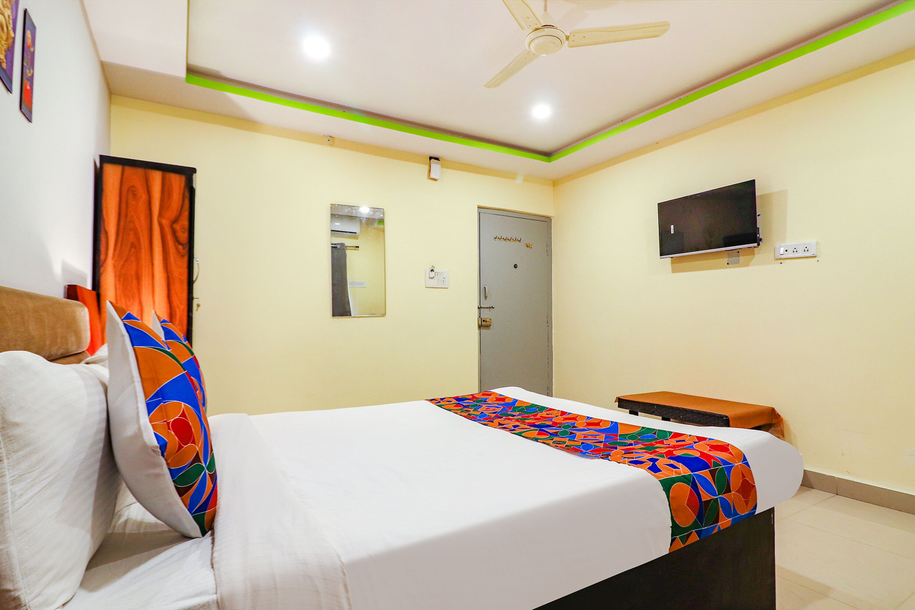 A hotel room with a bed, a TV, a ceiling fan, and a door.