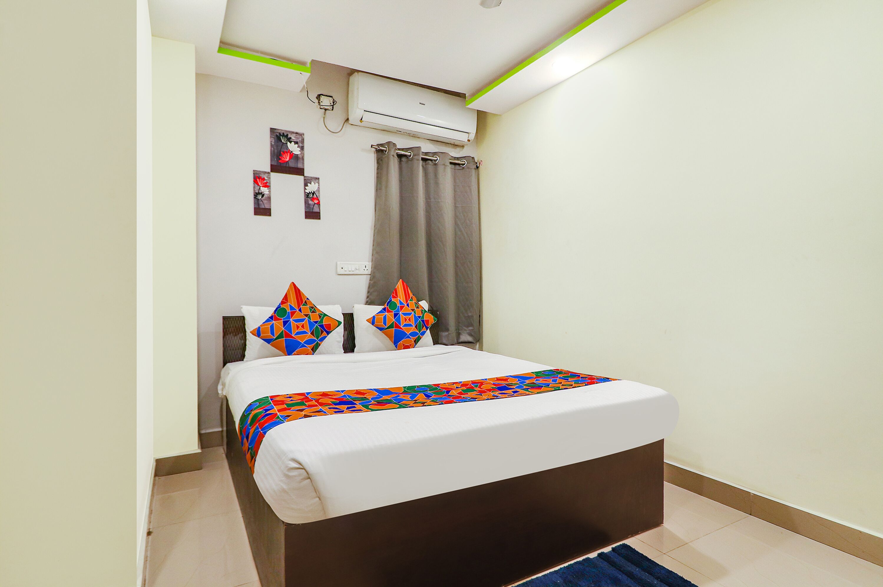 A neatly made bed with a colorful blanket, a wall-mounted air conditioner, and a curtain.