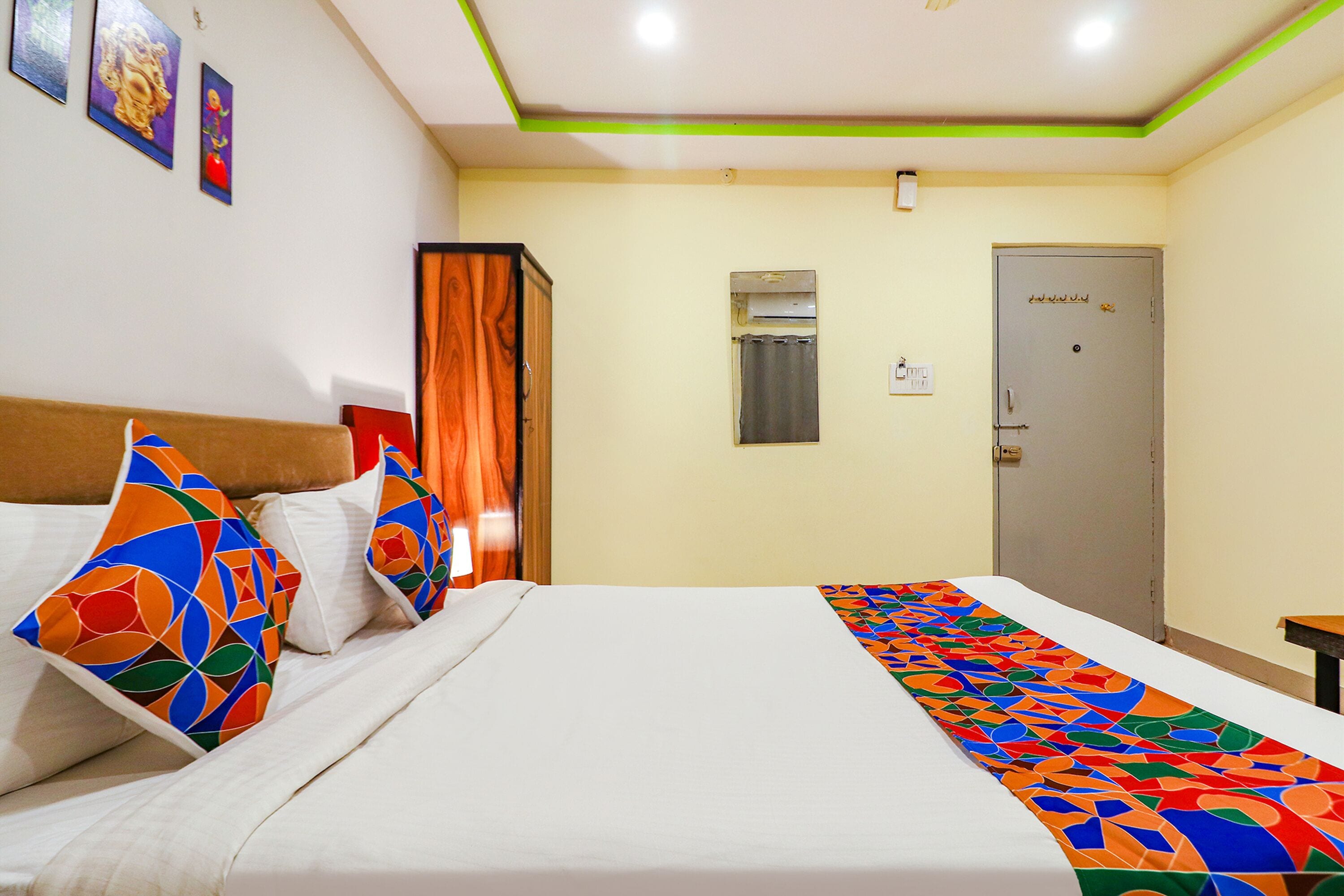 Une chambre d’hôtel avec un lit, des oreillers colorés, une porte et un climatiseur fixé au mur.