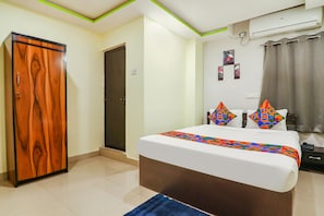 Quarto com guarda-roupa de madeira, cama com almofadas coloridas, tapete azul e ar condicionado fixado na parede.