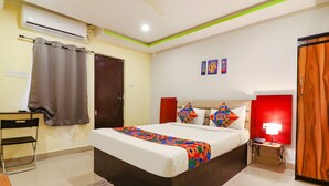 Quarto de hotel com cama, escrivaninha, cadeira, mesa de cabeceira, abajur e guarda-roupa.
