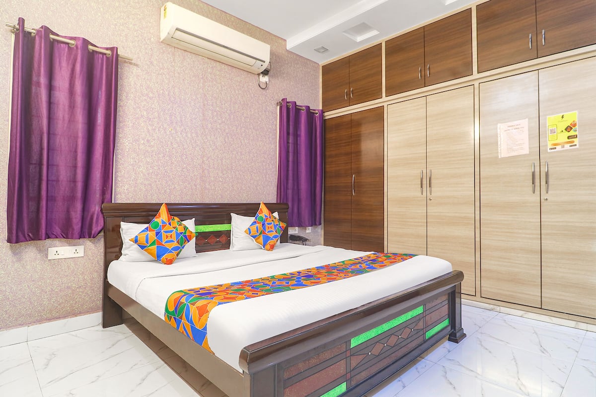 Quarto com cama, cortinas roxas, guarda-roupa de madeira e ar-condicionado fixado na parede.