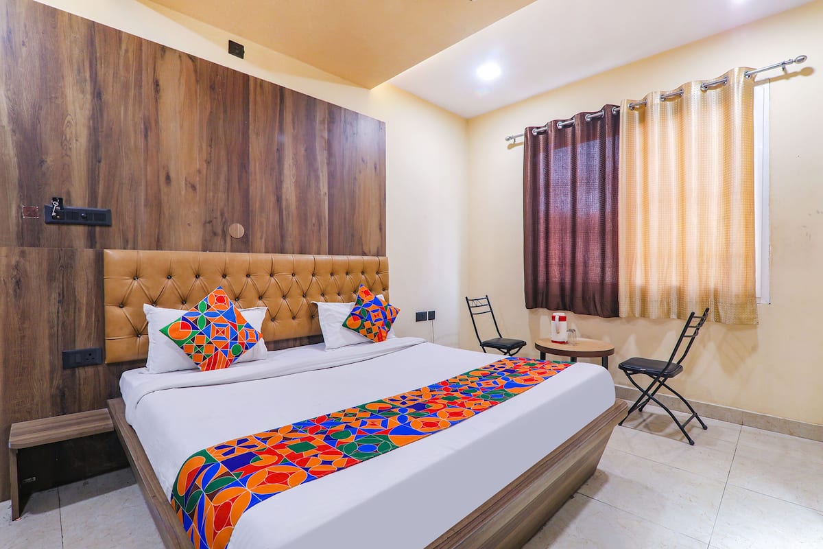 Habitación de hotel con una cama grande, cabecera de madera, una mesita con una silla y una ventana con cortinas.