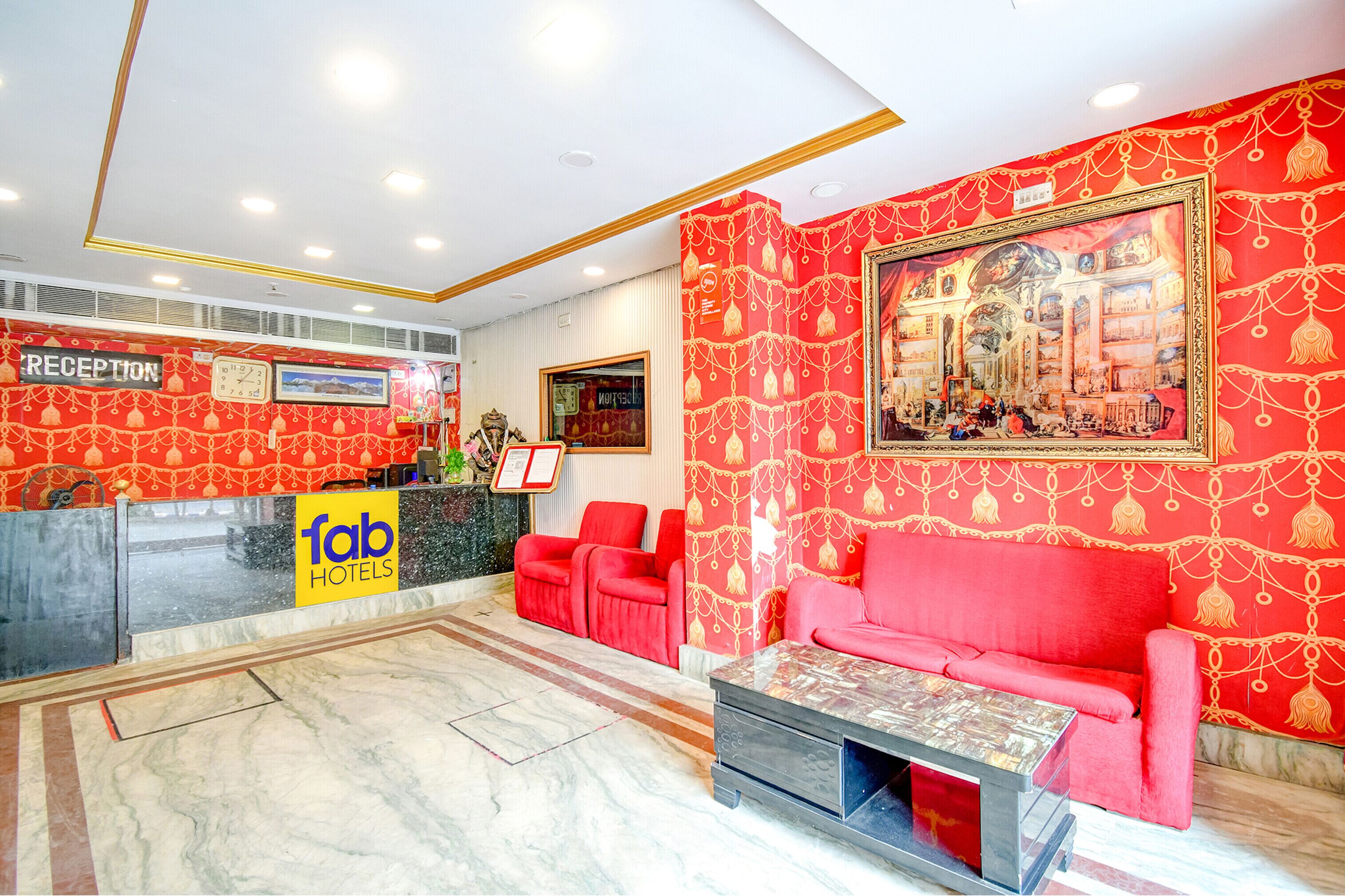 A hotel reception area with a reception desk, red seating, a coffee table, and a large framed painting on the wall.