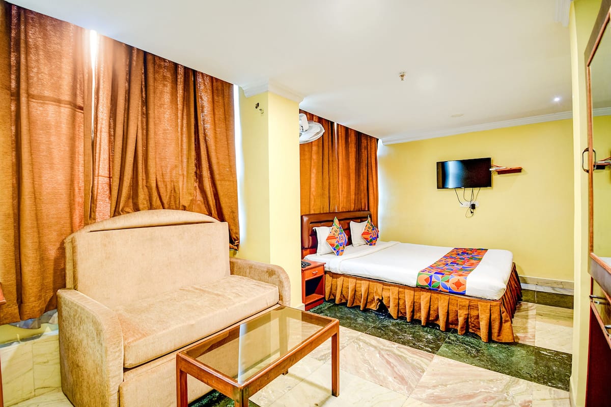 A hotel room with a sofa, a bed with a colorful bedspread, a flat-screen TV mounted on the wall, and a wooden nightstand.