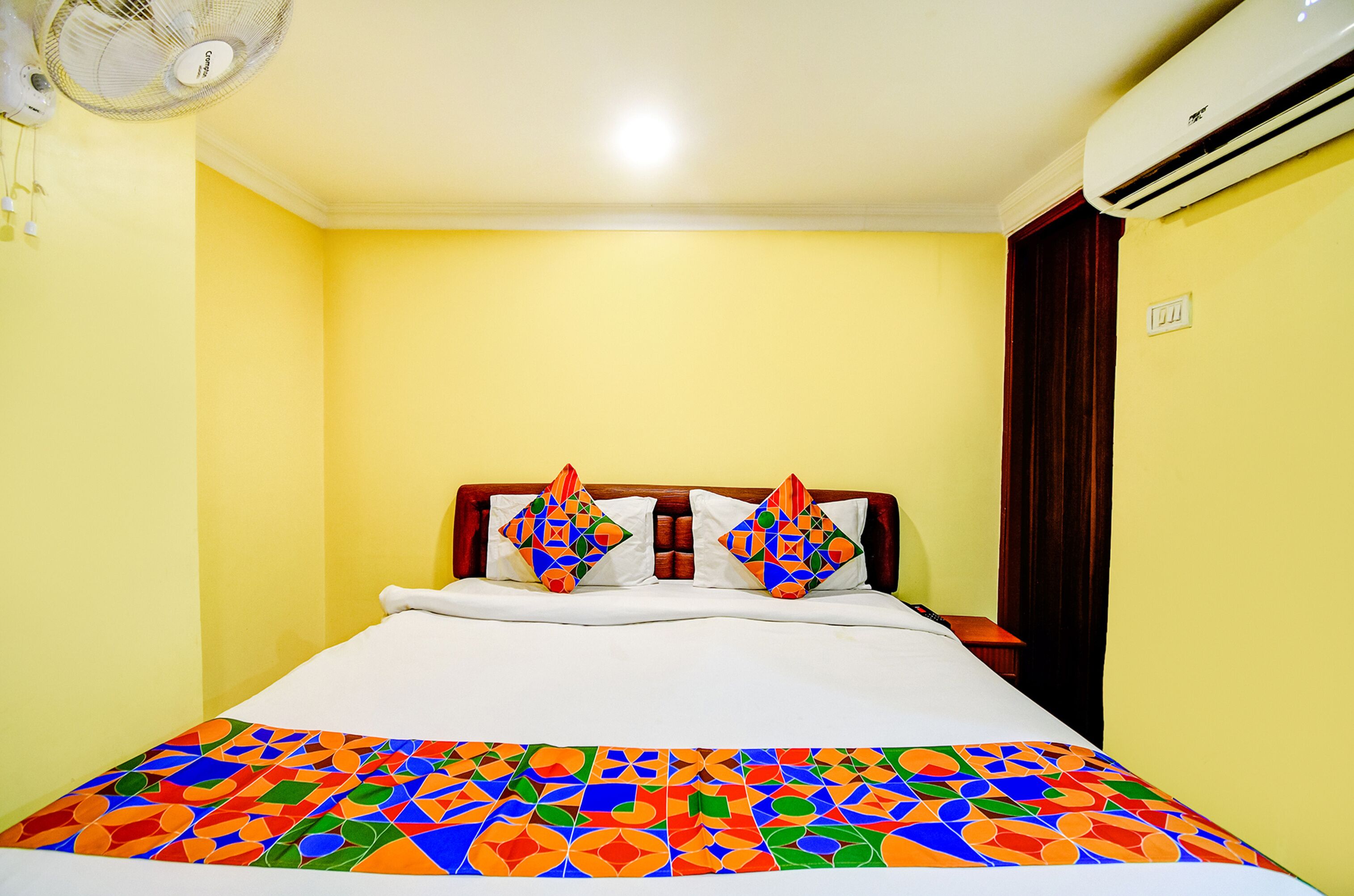 A hotel room with a bed, a ceiling fan, an air conditioner, and a window with curtains.