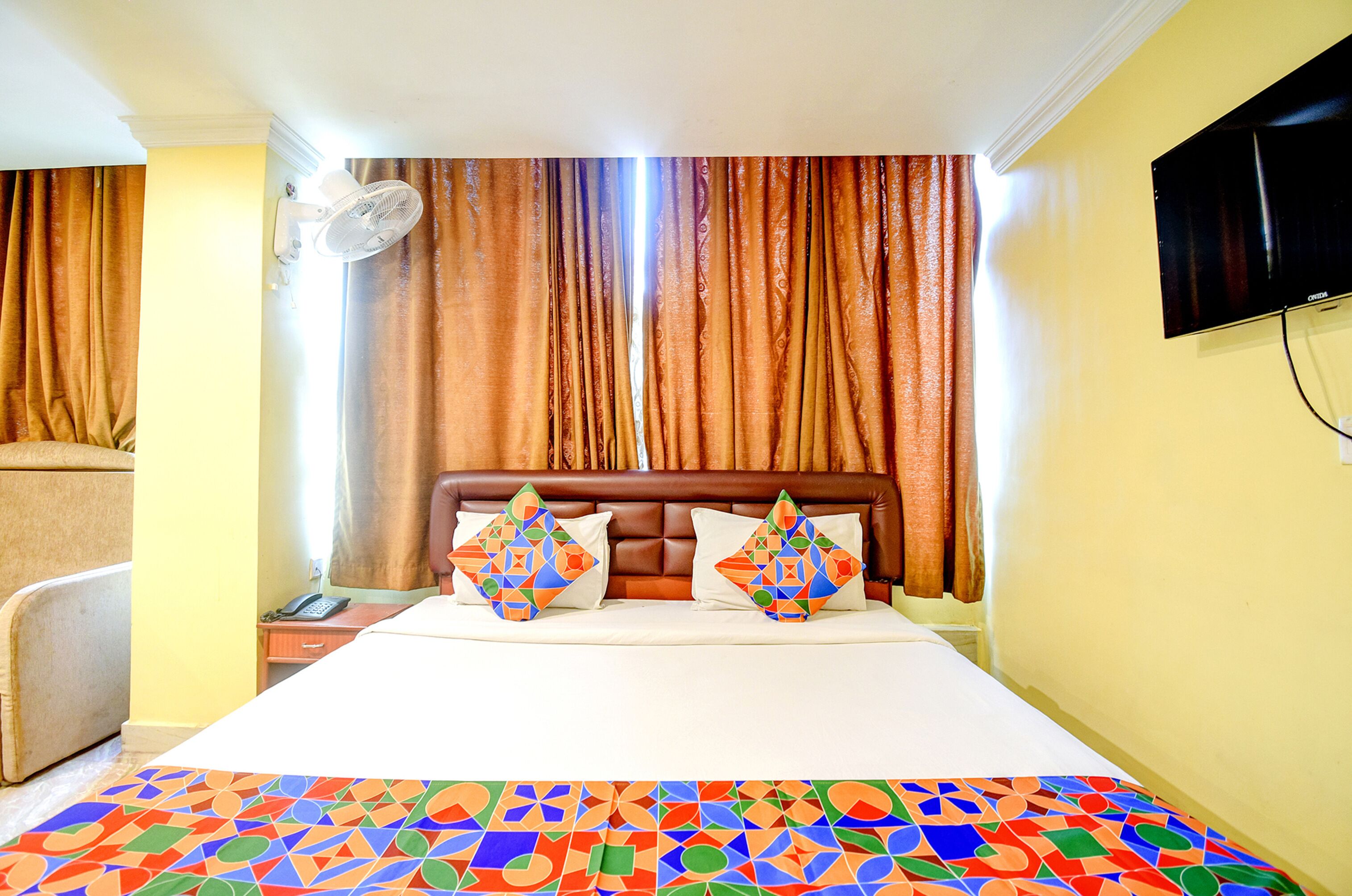 Habitación de hotel con cama, dos almohadas, mesita de noche, televisor y ventana con cortinas.