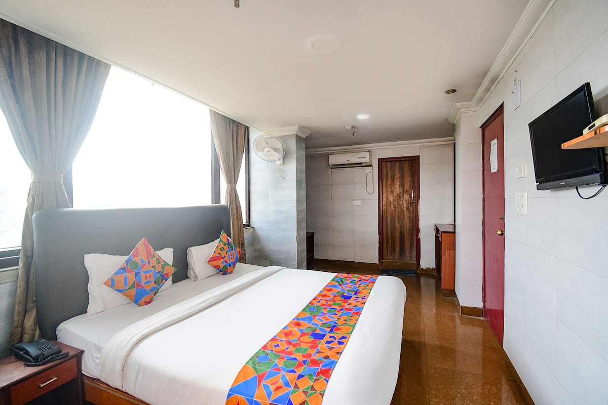 A hotel room with a large bed, a bedside telephone, an air conditioning unit, a television mounted on the wall, and a window with curtains.