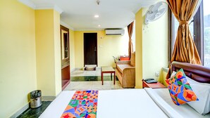 Una habitación de hotel con cama, escritorio, silla, ventilador y ventana con cortinas.