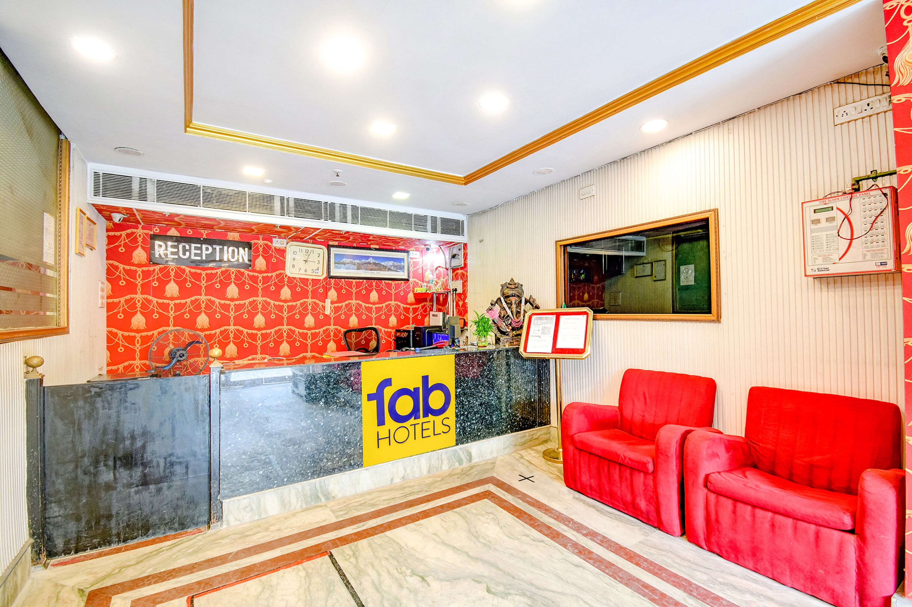 Uma área de recepção de hotel com balcão, relógio e sofá vermelho.