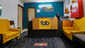 Un mostrador de recepción con un cartel que dice "fab hotels", dos sillones amarillos, una puerta de madera, una pared azul y un armario rojo.