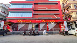 Un edificio de varios pisos con fachada roja, un letrero que dice 'Fab Hotels' en la parte superior y una tienda llamada 'Nazeer Foods' al frente.