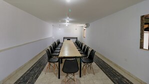 Un salón de conferencias con una larga mesa y sillas, paredes blancas y suelo de baldosas.