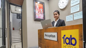 Een receptiebalie bij Fab Hotels, met een klok, een lijst en een bord waarop de inchecktijden staan.