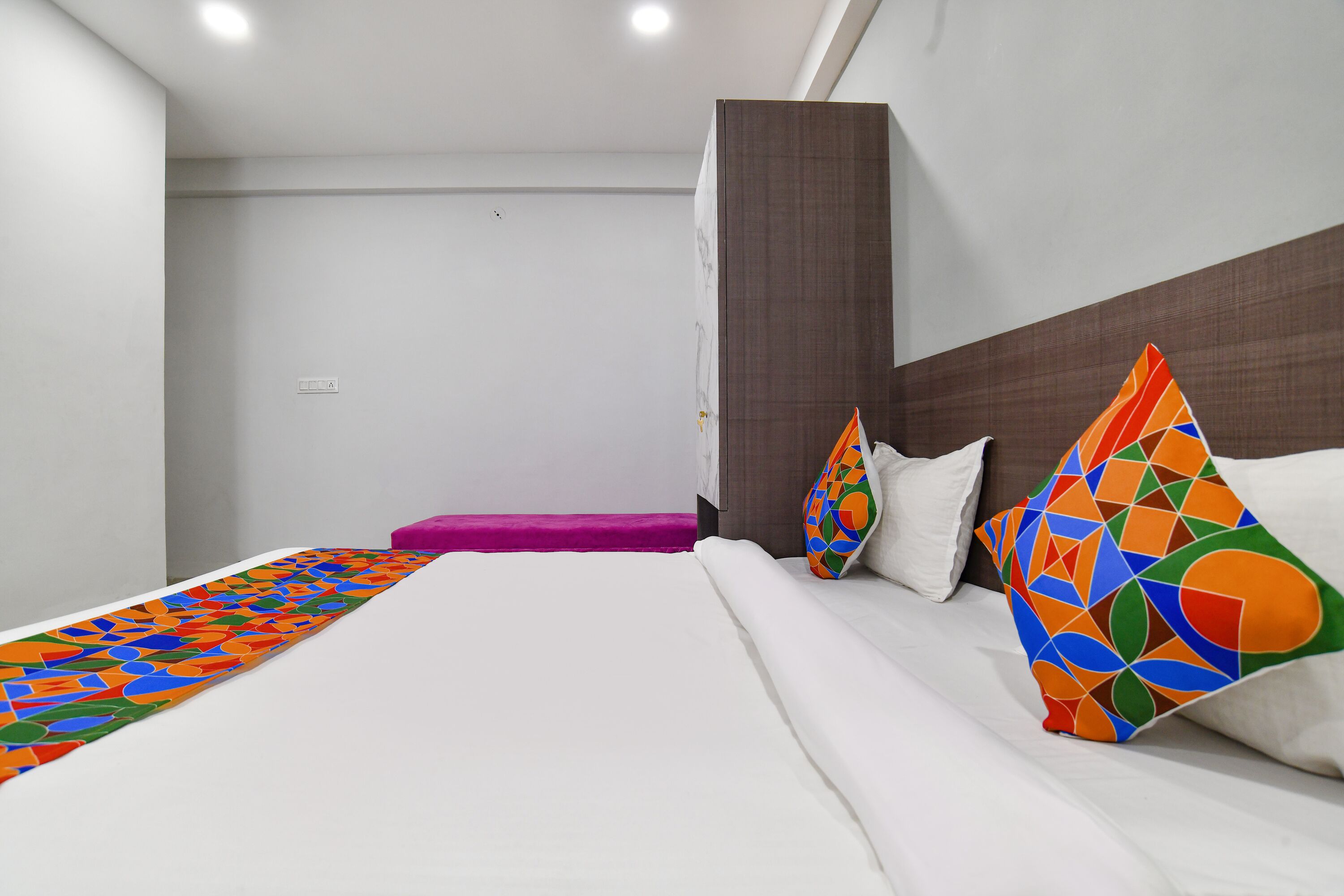 Ett modernt hotellrum med en stor säng, en sänggavel i trä och färgglada, geometriska kuddar.